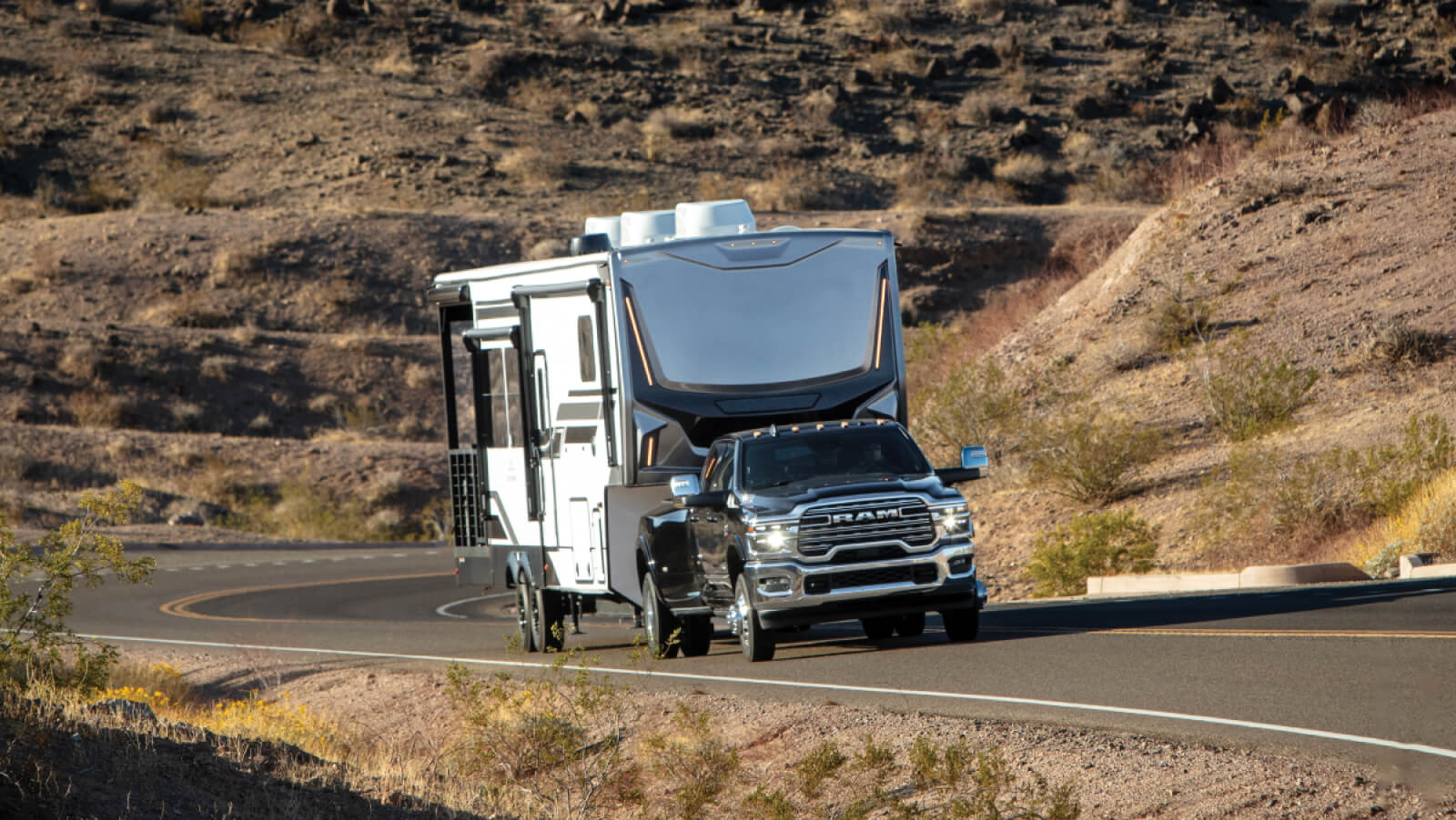 2026 3500 Limited in Diamond Black Crystal Pearl towing a large camping trailer uphill on a winding country road
